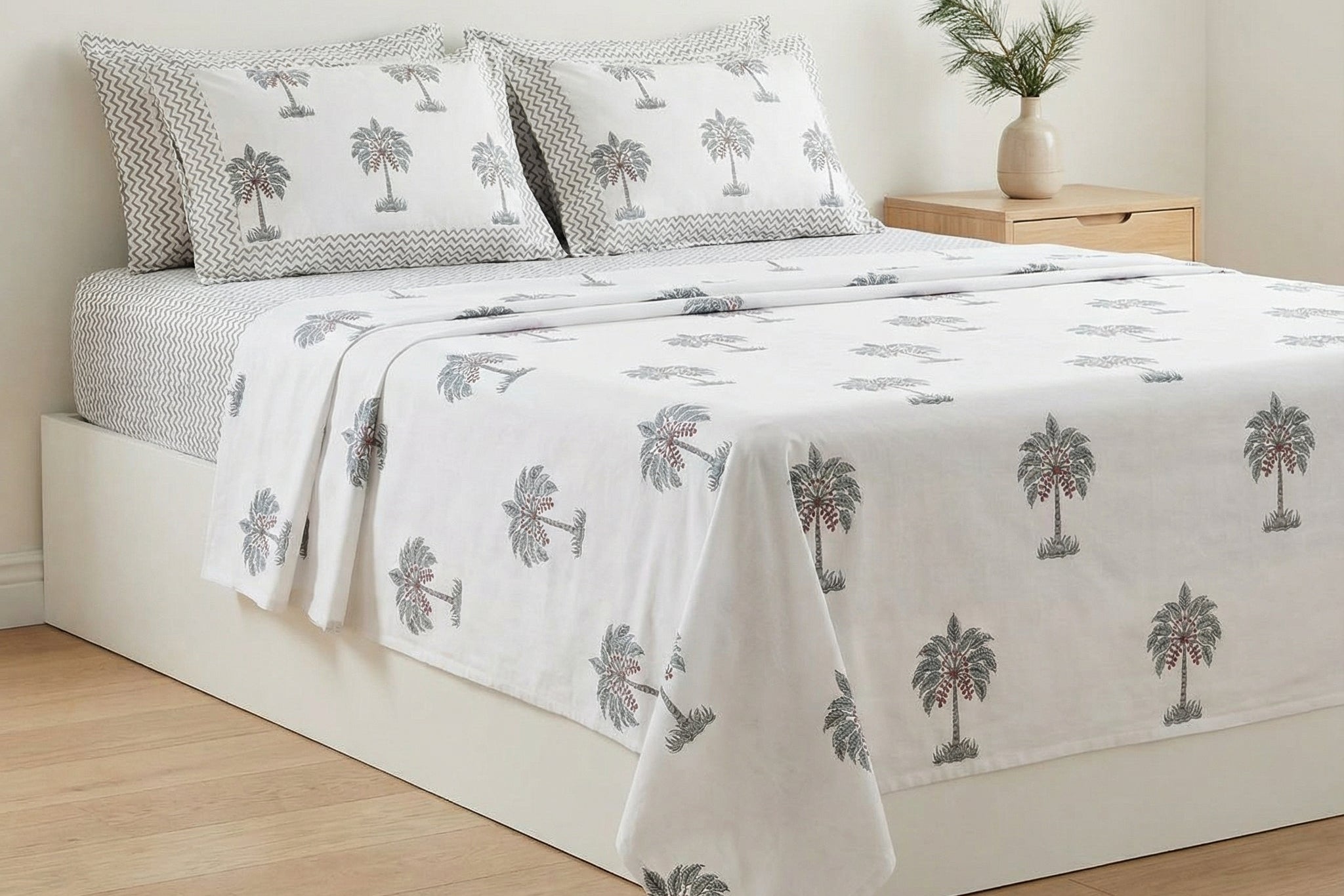 Bed with palm tree patterned bedding in a room with a wooden floor and white walls.